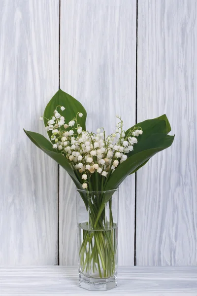 White lilies of the valley in a glass on a wooden boards — Stock Photo, Image