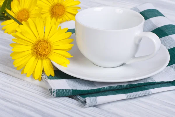 White cup and saucer with bouquet of daisies on a wooden table — Stock Photo, Image