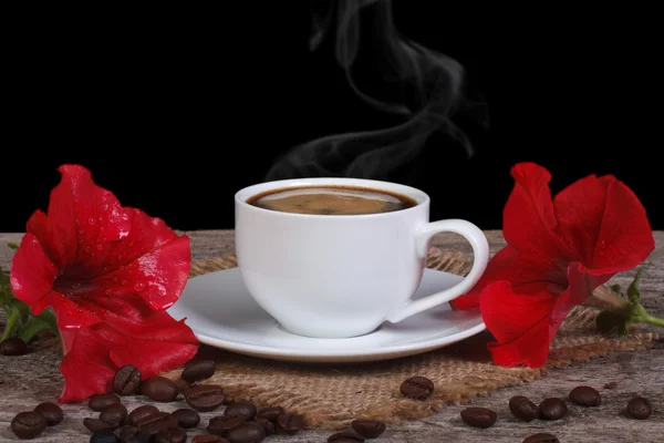 Hot coffee and red petunia flowers on a wooden table. low key — Stock Photo, Image