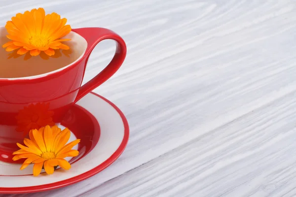 Herbal tea with calendula flowers in a red cup on the table — Stock Photo, Image