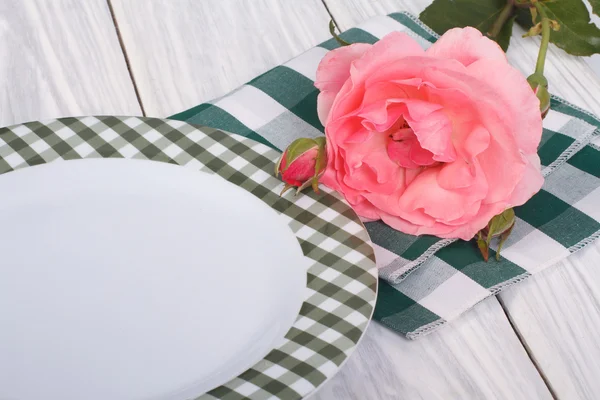 Ρύθμιση του πίνακα. όμορφο ροζ τριαντάφυλλο και ένα πιάτο στο τραπέζι — Φωτογραφία Αρχείου