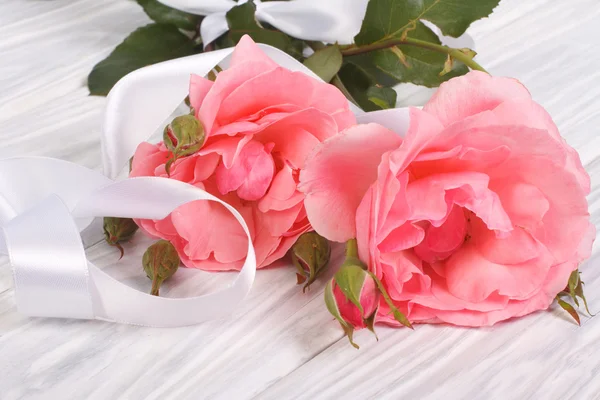 Розовые розы с белой лентой на деревянном столе — стоковое фото
