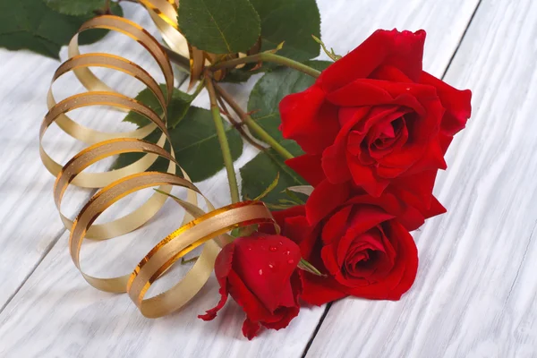 Red roses with gold ribbon on background wooden table — Stock Photo, Image