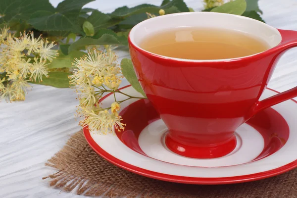 Tè alle erbe con lime in una tazza rossa su un tavolo di legno — Foto Stock