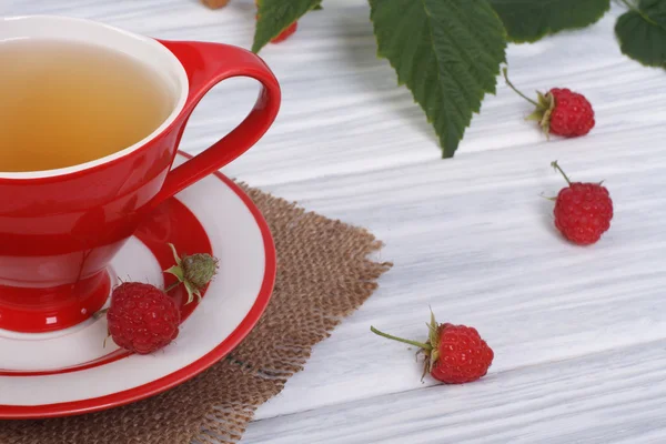 Tea with raspberries in a red cup on the table — Stock Photo, Image