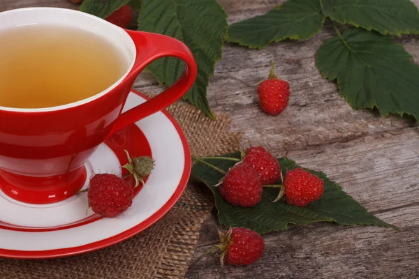 Tea with raspberries in a red cup on old wooden table — Stock Photo, Image