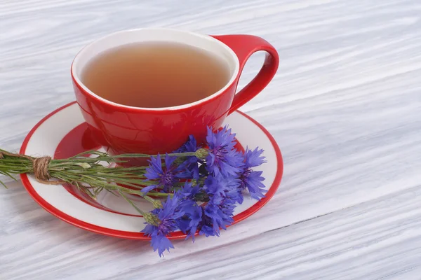 Травяной чай в керамической чашке и васильковые цветы на столе — стоковое фото