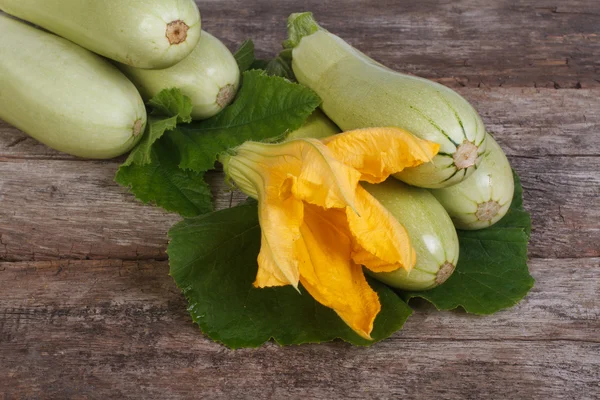 Färsk zucchini med blad och blommor på en planka — Stockfoto