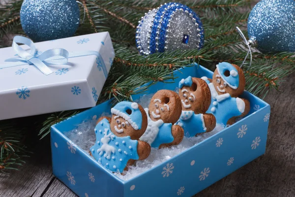 Gingerbread men in blue gift box on the background of Christmas balls and tree — Stock Photo, Image