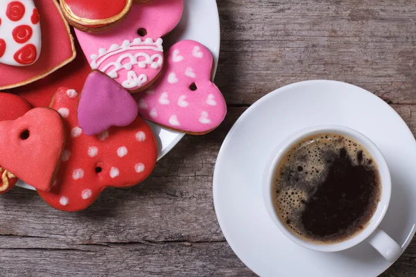 Caffè nero e biscotti di cuore colorati su un tavolo di legno Foto Stock Royalty Free