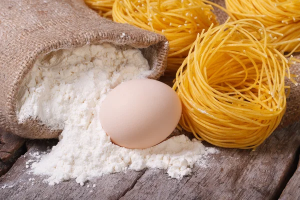 Сухая паста в виде гнезд, сырое яйцо и мешок муки — стоковое фото