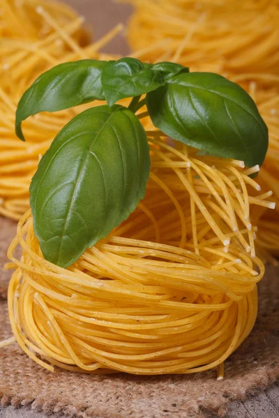 Nido de pasta seca primer plano con albahaca verde en la mesa . — Foto de Stock