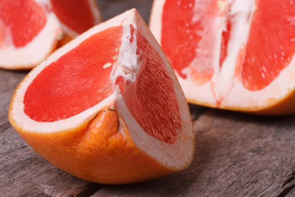 Pieces of red grapefruit on the old wooden table closeup — Stock Photo, Image