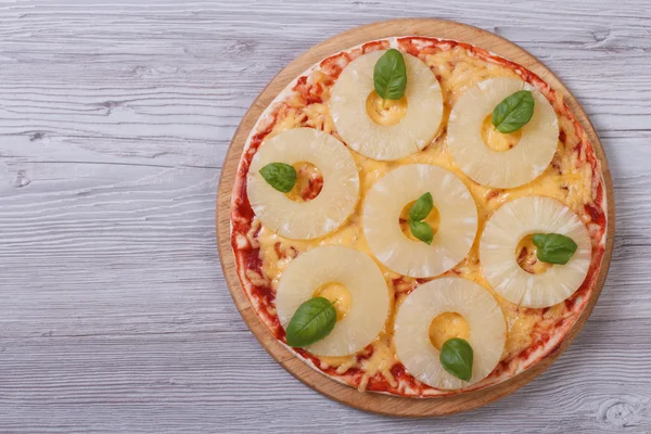 Pizza with pineapple rings and basil on the table