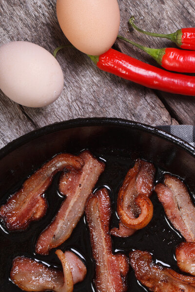 жареный бекон в сковороде и чили, яйца на столе
