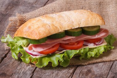 ciabatta sandwich with ham and vegetables on an old wooden table clipart