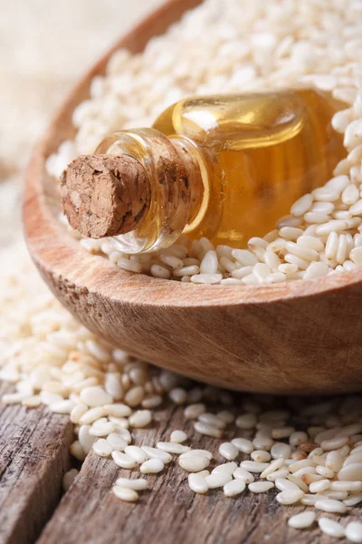 Sesame oil in a glass bottle and seeds in a wooden bowl — Stock Photo, Image