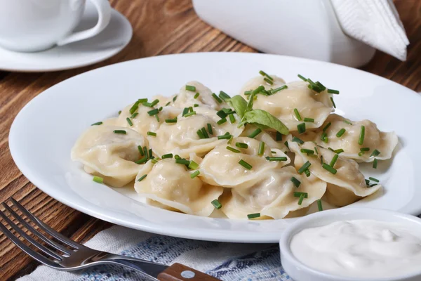 Dumplings med gräddfil på en vit platta med lök gräslök — Stockfoto