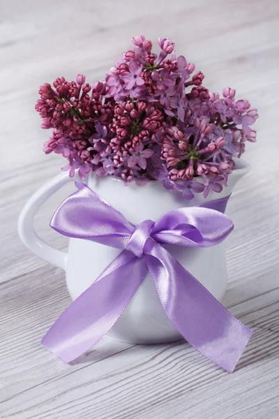 Delicate flowers of lilac in a white jug with a bow — Stock Photo, Image