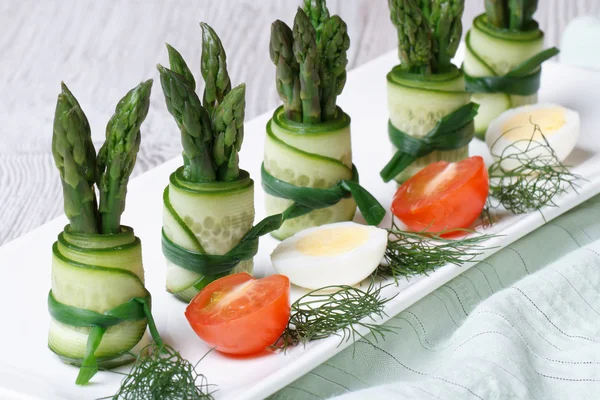 Bir plaka üzerinde yeşil kuşkonmaz ile taze salatalık ruloları — Stok fotoğraf