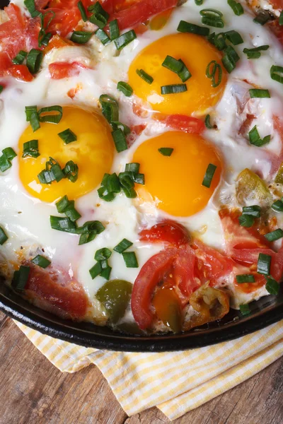 Fried eggs with tomatoes in a pan on the table vertical  macro — Stock Photo, Image