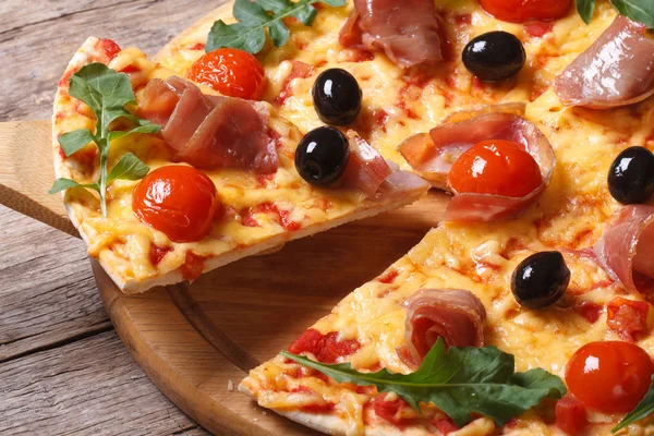 Piece of pizza with ham, tomatoes, black olives and arugula — Stock Photo, Image