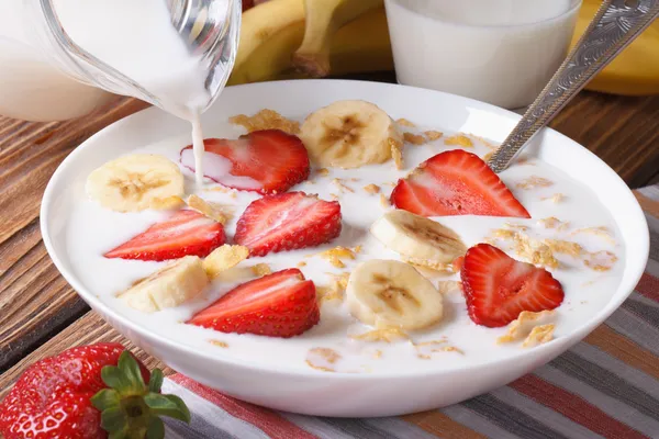 Muesli con fresas, plátano y leche se vierte de una jarra — Foto de Stock