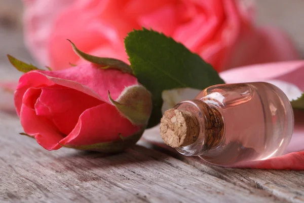 Olio di rosa in bottiglia di vetro e fiori rosa sul tavolo di legno — Foto Stock