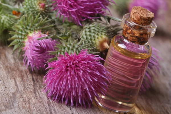 Burdock oil in a glass bottle on a background of flowers — Stock Photo, Image