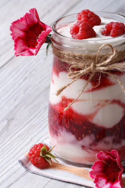 Delicious raspberry yogurt in a glass jar closeup and flowers — Stock Photo, Image