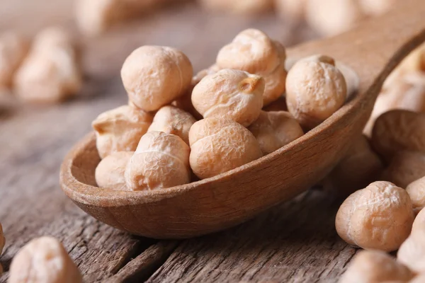 Garbanzos crudos en una cuchara de madera macro y dispersos —  Fotos de Stock