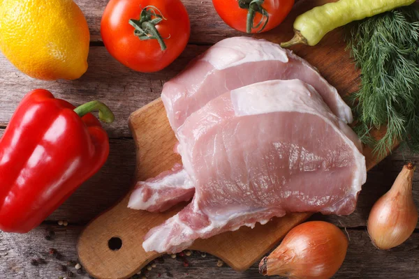 Carne de porco crua em uma tábua de corte e legumes frescos vista superior — Fotografia de Stock