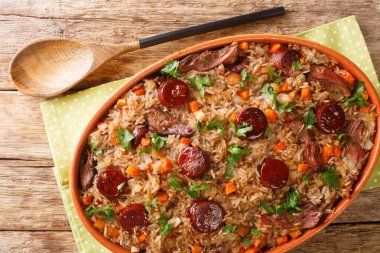 Portekiz ördeği pirinç arroz de pato kırmızı şarap, soğan, havuç ve sucukla pişirilmiş ahşap masadaki fırın kabında yakın çekim. Yukarıdan yatay üst görünüm