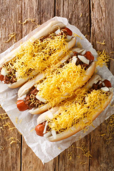 Вкусный домашний хот-дог Цинциннати с сосисками из говядины, сыром чеддер и луком крупным планом в газете. Вертикальный вид сверху с бова