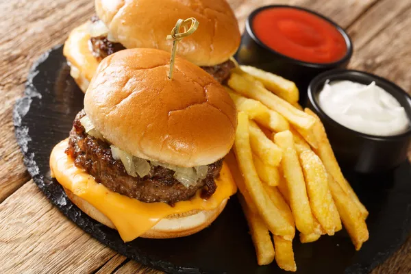 Biftek, soğan ve peynirli tereyağlı Amerikan hamburgerleri masada patates kızartması ve sosla servis ediliyor. yatay