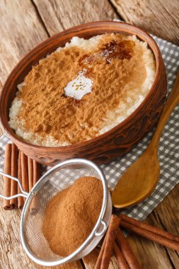 Üzerinde tarçın, şeker ve tereyağı olan sütlaç masanın üstünde. dikey