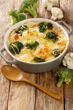 Karnabahar ve brokoli, ahşap bir masadaki kapta peynir sosuyla pişirilmiş. Dikey