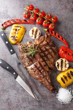 Izgarada pişirilmiş sulu büyük biftek ve beton gri arka planda yakın plan ızgara sebzeler. Yukarıdan dikey üst görünüm