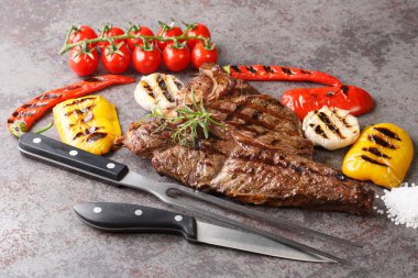 Izgara biftek, sarımsak, biber ve domatesle birlikte beton gri arka planda. yatay