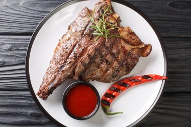 Sulu büyük bir biftek, otlarla ızgara, domates sosu ve ahşap bir masada yakın plan kırmızı biber. Yukarıdan yatay üst görünüm