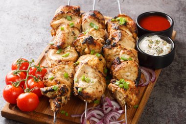 Juicy grilled chicken skewers with fresh vegetables and two sauces close-up on a wooden tray on a gray concrete background. horizonta