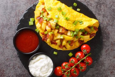 Çiftçi omleti, kızarmış patates ve domuz pastırması ile birlikte beton bir masada tahtaya yakın plan sosla servis edilir. Yukarıdan yatay üst görünüm