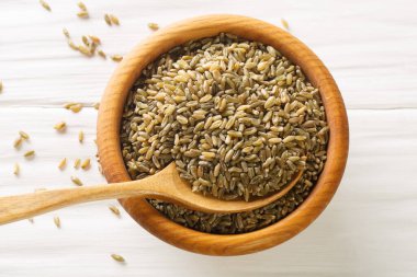 Pişmemiş, çiğ freekeh ya da firik, kavrulmuş buğday tanesi, ahşap tabakta, ahşap kaşık ve beyaz kırsal masa. Yukarıdan yatay üst görünüm