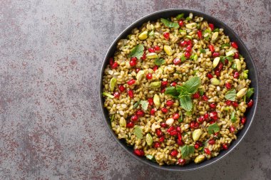 Sehpadaki tabakta nar, fındık ve otlarla nefis vejetaryen freekeh. Yukarıdan yatay üst görünüm