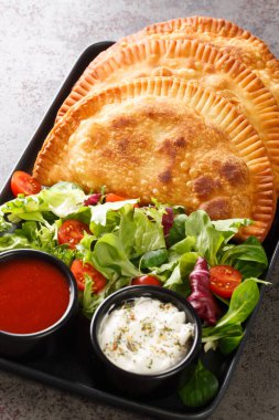 Geleneksel Chebureki, taze salata ve soslarla servis edilen et tabağında servis edilir. Dikey