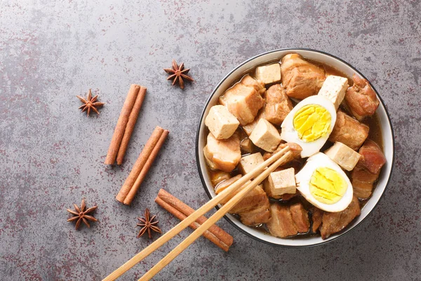 Kai Palo popular Thai cuisine has an easy menu serving hard boiled egg and pork belly and Tofu over soy broth closeup in the bowl on the table. Horizontal top view from abov