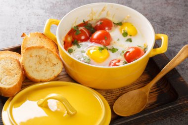 Beyaz ahşap masada seramik kootta pişmiş yumurta, masadaki ahşap tepside kahvaltı. Yatay