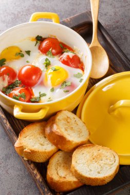 Peynirli yumurtalı cocotte ve taze maydanozla servis edilen sebzeler ve masadaki ahşap tepside yakın plan tost. Dikey