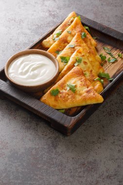 Masadaki ahşap tepsinin üzerine ekşi kremayla servis edilen üç köşeli kızarmış krep. Dikey