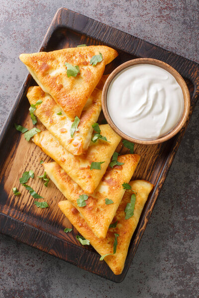 Ukrainian triangular fried pancakes benderyki served with sour cream close up on a wooden tray on the table. Vertical top view from abov